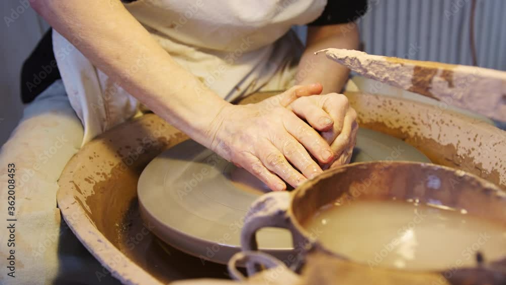 Close up of male potter throwing clay for pot onto pottery wheel in ceramics studio - shot in slow motion Close up of male potter throwing clay for pot onto pottery wheel in ceramics studio - shot in slow motion