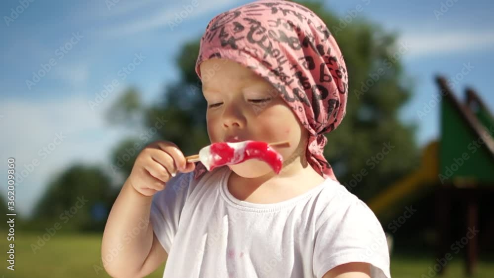 Cute girl in pink bandana enjoy eating red ice cream on a hot summer sunny day. Happy childhood and travel concept. Portrait against the sky Cute girl in pink bandana enjoy eating red ice cream on a hot summer sunny day. Happy childhood and travel concept. Portrait against the sky
