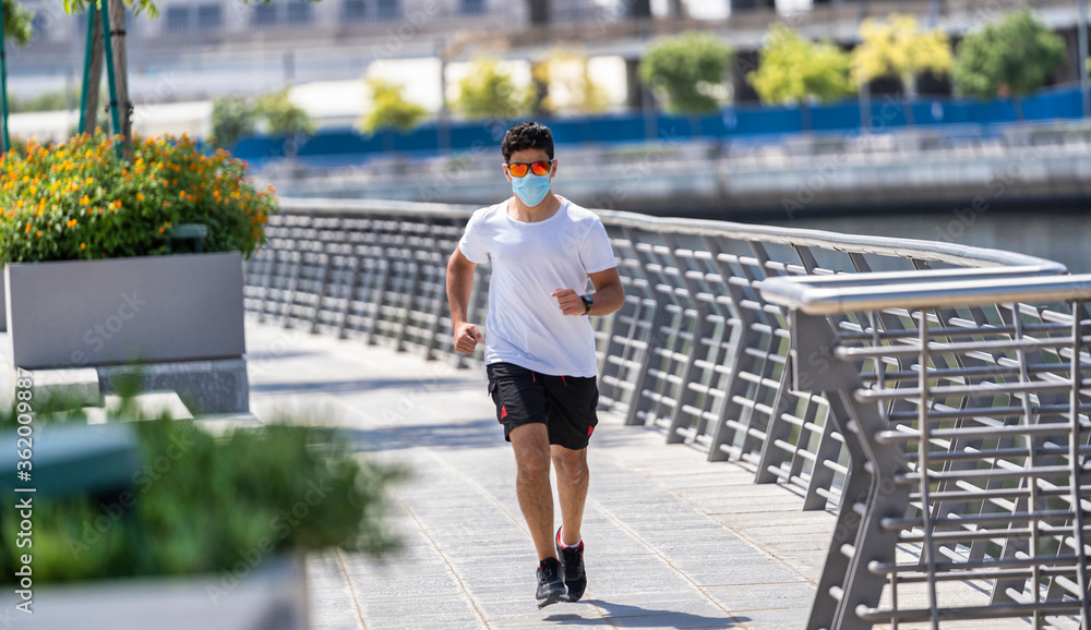 Morning run, a man with medical mask runs along the road with a beautiful view of Dubai. UAE, fitness, sport, exercising and healthy lifestyle concept.