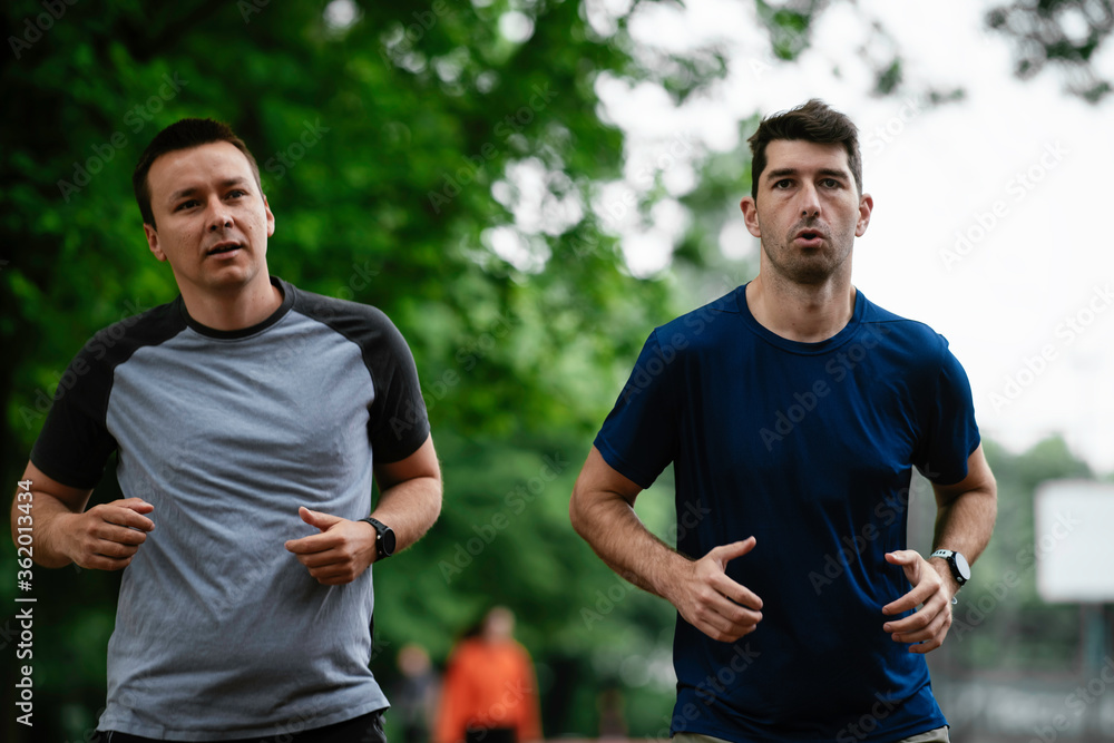Young men training on a race track. Two young friends running on the athletics track Young men training on a race track. Two young friends running on the athletics track