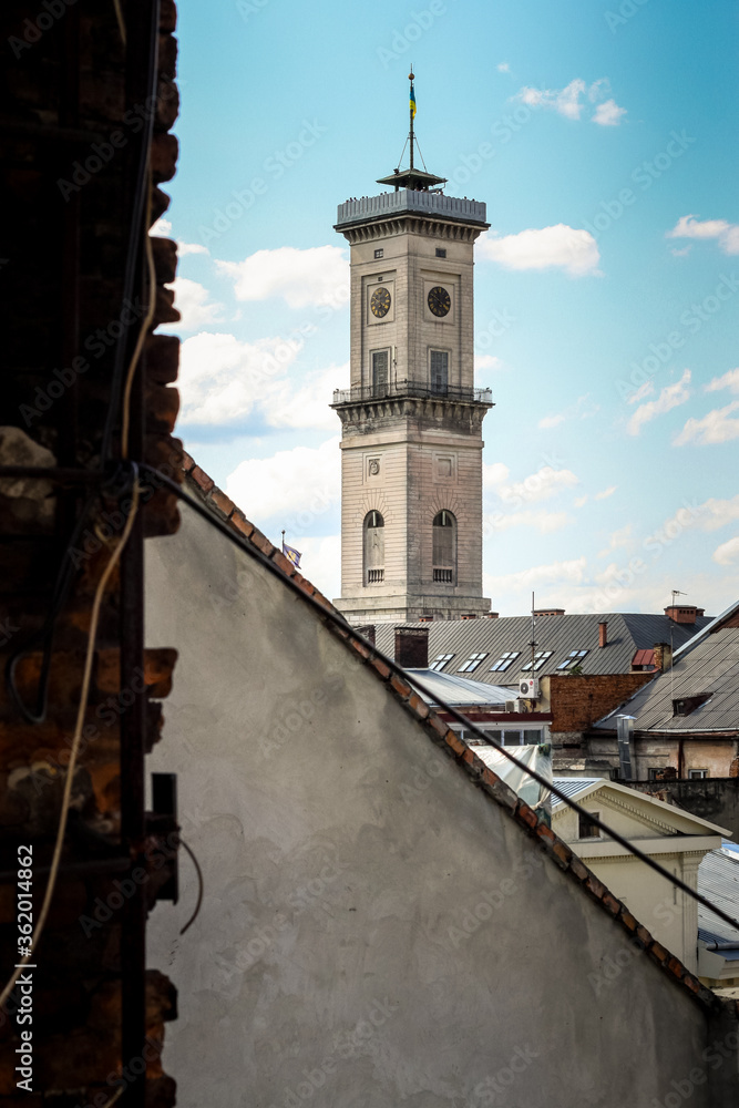 vertical view from rooftop on Lviv town hall tower against blue sky with white clouds