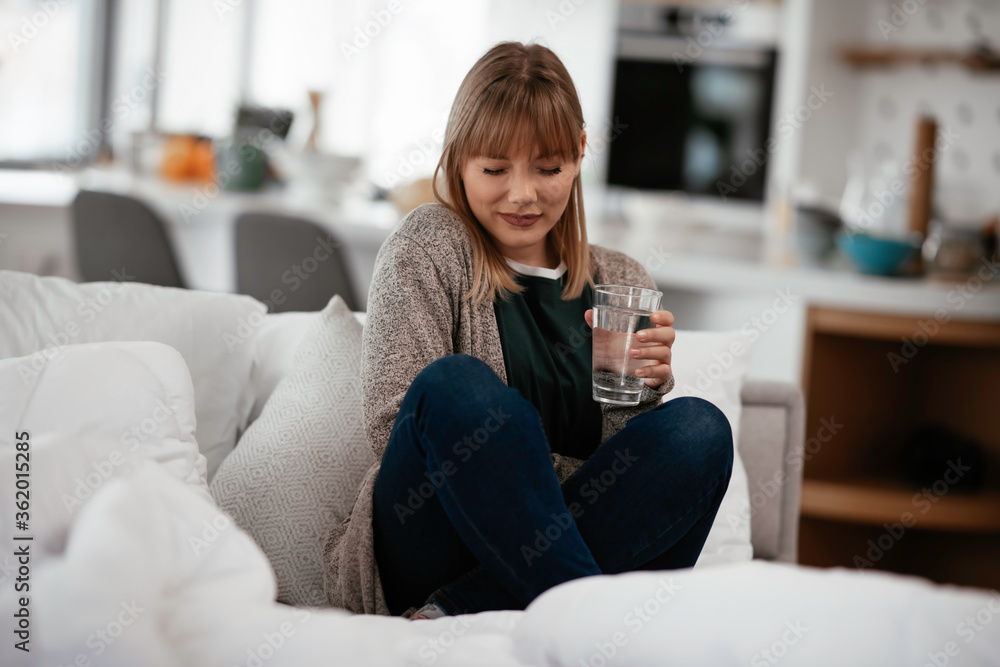 Young sick woman taking medicine pill. Beautiful woman sitting on sofa having stomach pain. Young sick woman taking medicine pill. Beautiful woman sitting on sofa having stomach pain.