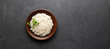 Boiled rice in a brown plate on black concrete background. Asian food. Top view with copy space.
