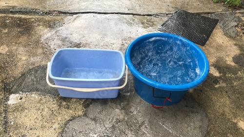 Blue tank has a lot of water in a rainy day,on cement floor,while it rains,we can take can bring containers to support rainwater,to keep it.Save water,save environment concept