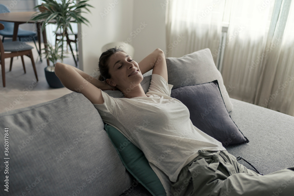 Happy woman lying on the sofa at home and relaxing - obrazy, fototapety, plakaty 