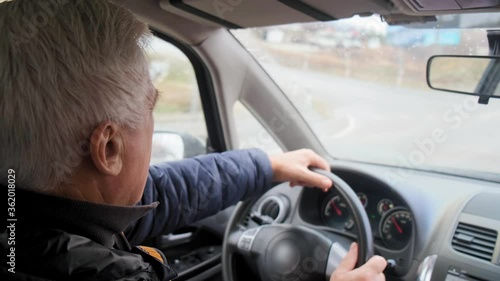 aged man with grey hair drives car with hands on black leather steering wheel on rainy autumn day slow motion closeup