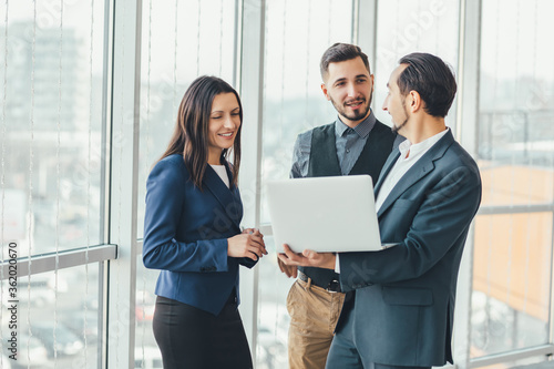 Three successful business people talking in office, analysing some data in laptop.