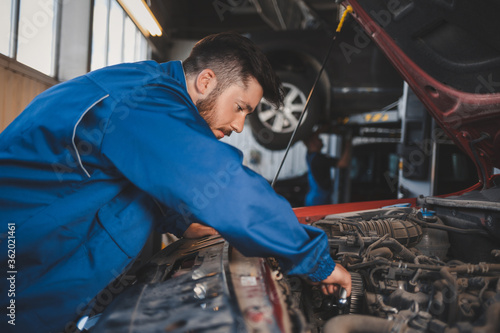 Male auto mechanic in blue uniform is repairing a car