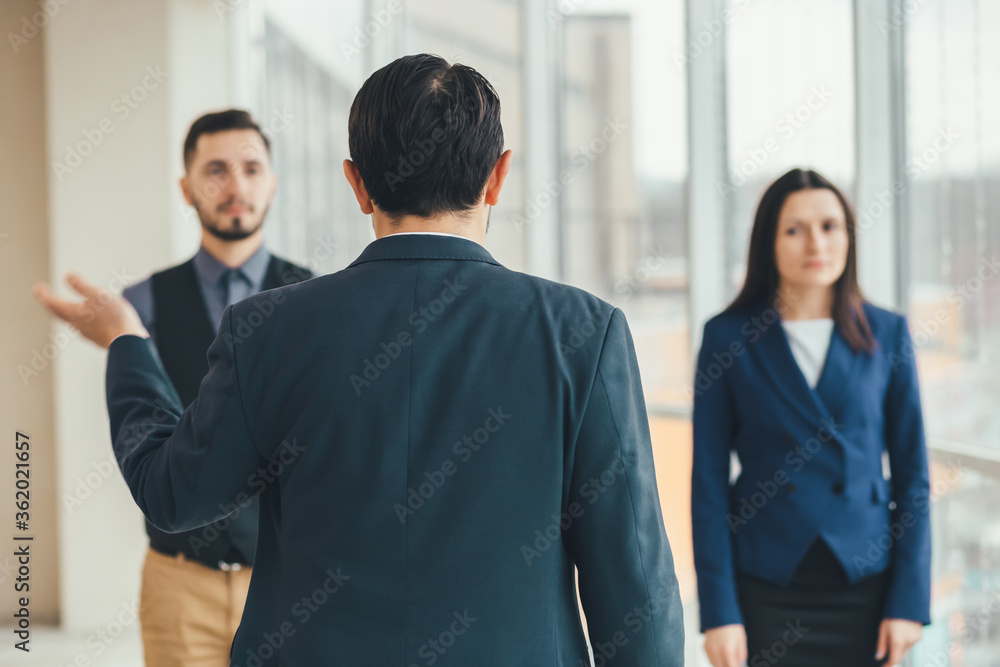 Angry boss standing back to the camera, shouting at his workers, raising hand, while stressed employees standing, with guilty look on their faces. Angry boss standing back to the camera, shouting at his workers, raising hand, while stressed employees standing, with guilty look on their faces.
