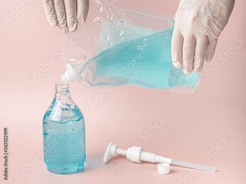 Hands with gloves refill blue alcohol gel into plastic bottle. Pink pastel background. photo
