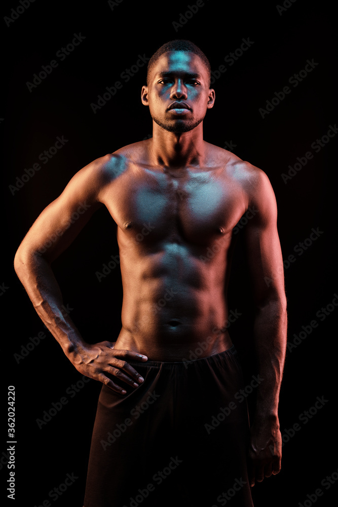 Naklejka premium Standing black man looking at camera lit with colored lights