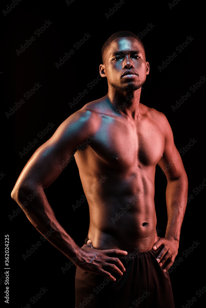 Standing black man looking at camera with his hands on his hips lit with colored lights