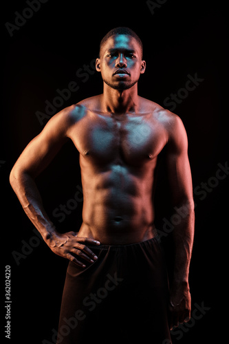 Standing black man looking at camera lit with colored lights