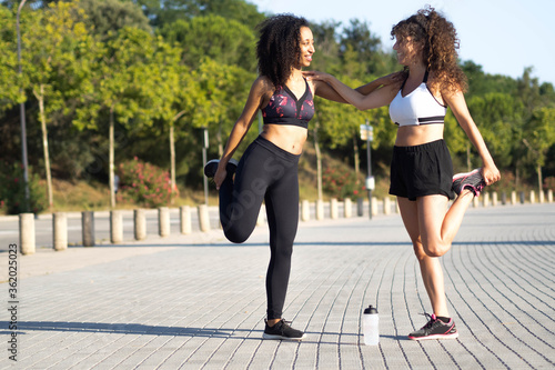 Two multi-ethnic girlfriends doing stretching with runner clothes. Sportswomen