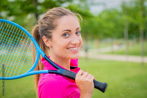 Portrait of tennis player girl holding racket outside - Portrait beautiful blonde girl who is playing tennis in stylish sportswear holding racket in hand, preparing to play tennis outdoors