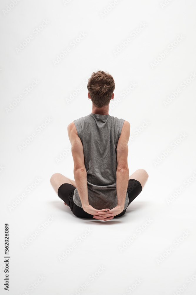 Fototapeta premium Young boy streching his arms with his legs crossed on white background