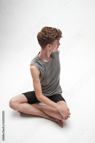 Young boy stretching with his body turned to his right and legs crossed on white background © Manuel