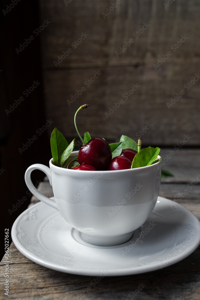 Sweet cherries in a white tea cup on wooden rustic background Sweet cherries in a white tea cup on wooden rustic background