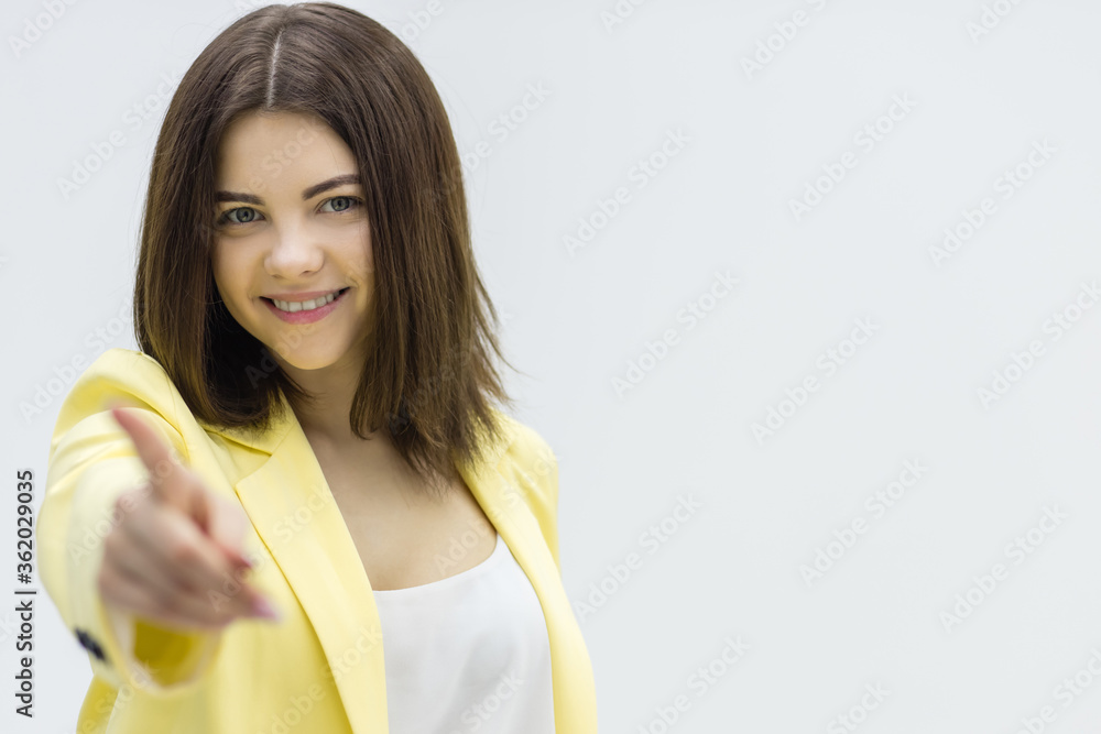 Young woman pointing at you and looking at camera, smiling.