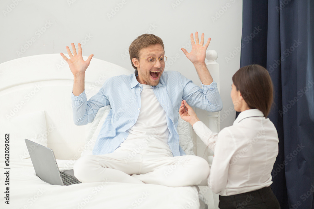 Woman proposing to man in bedroom. Handsome man with crazy face expression being surprised by his girfriends proposal.