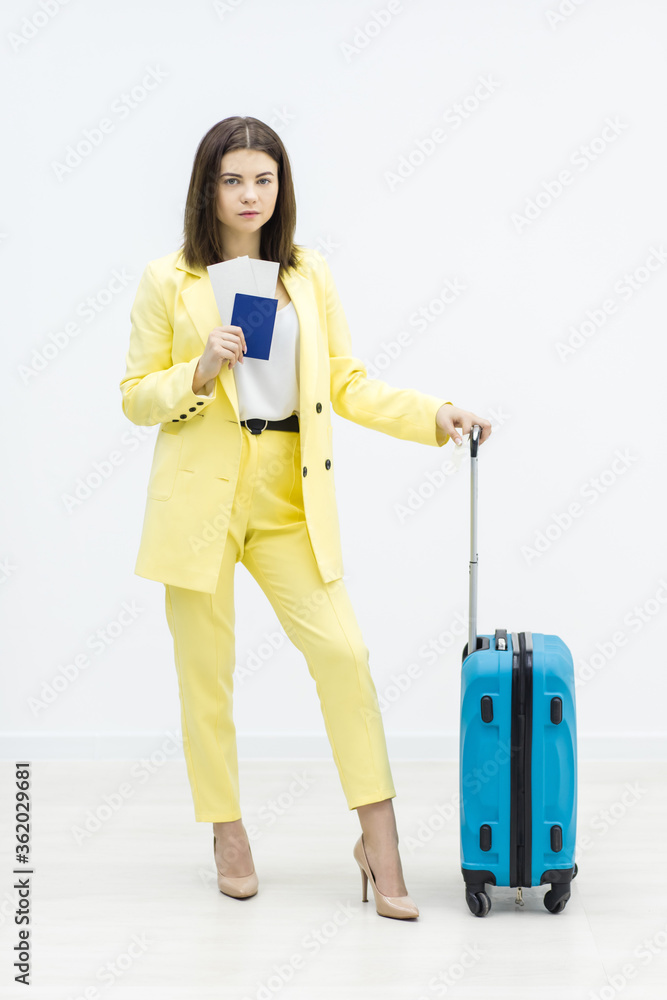 Businesswoman going on business trip. She stands with passport in hand and blue suitcase on her side. Businesswoman going on business trip. She stands with passport in hand and blue suitcase on her side.