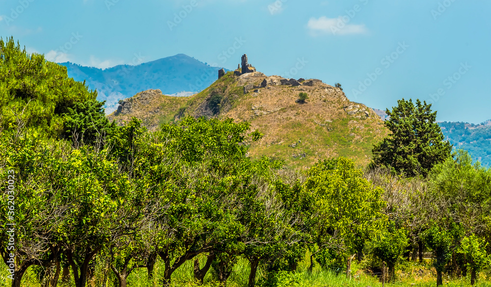 A view across an orchard to a hill top ruin in the foot hills of Mount Etna, Sicily in summer