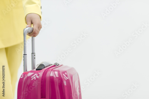 Cropped shot of female hand carrying a pink suitcase over white background with copyspace. © Andrii