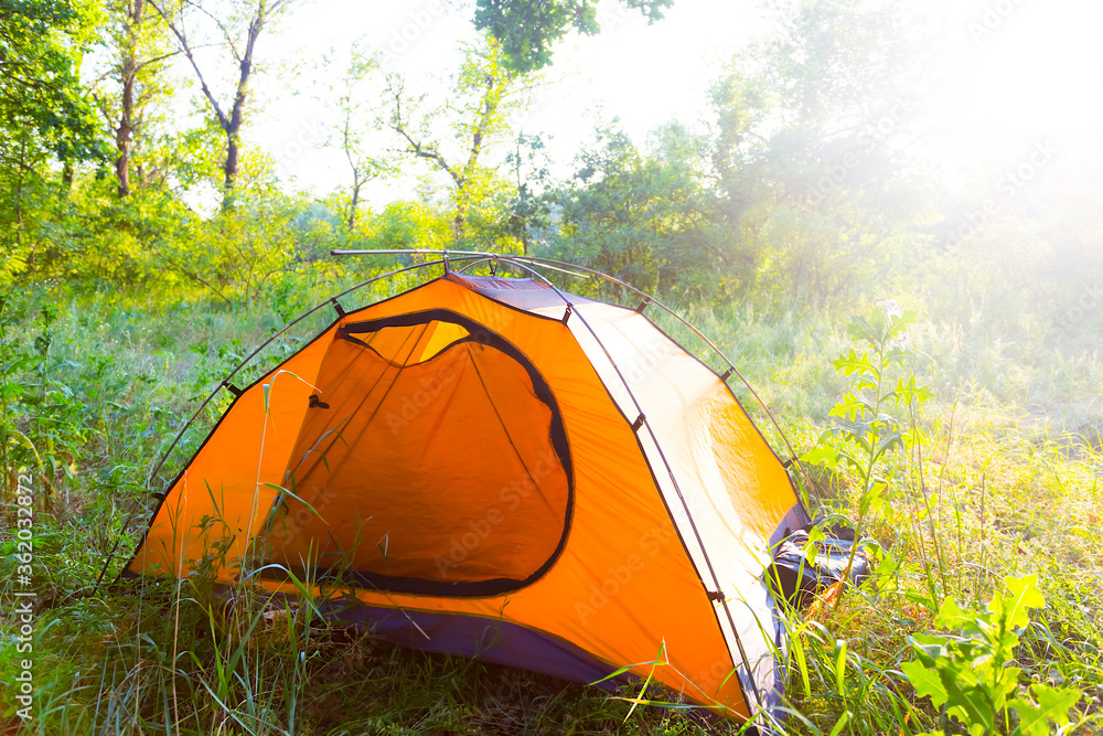 closeup orange touristic tent on a forest glade in a light of sun, travel background