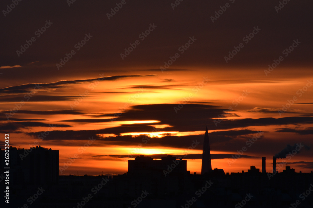 Colorful sunset with cloudy sky, city silhouette with high-rise and factory on foreground