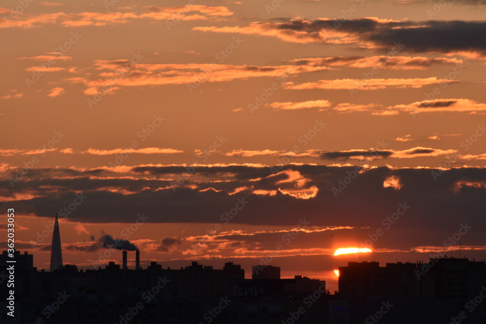 Sunset in pink with sun, cloudy sky and city silhouette with high-rise and factory on foreground