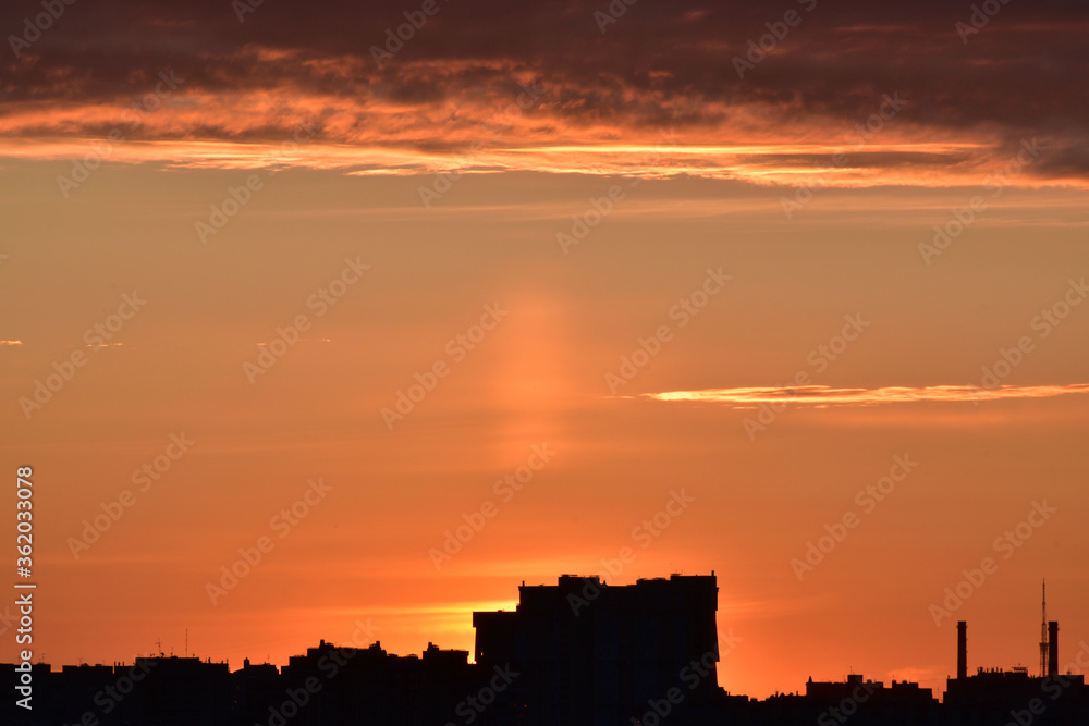 Colorful sunset with slightly overcast sky and city silhouette on foreground