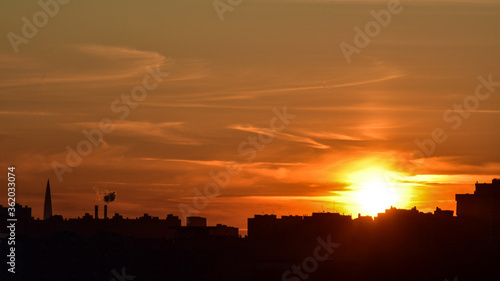 Colorful sunset with sun, slightly overcast sky and city silhouette on foreground