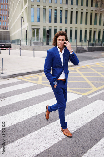 Full length portrait of a handsome businessman talking on his mobile phone while cross the pedestrian of big city street © BullRun