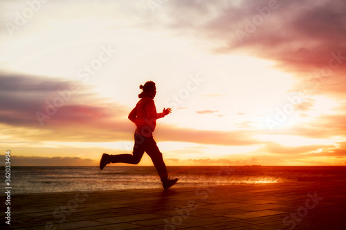 Silhouette of male athletic man running fast along seashore with amazing sky view on background