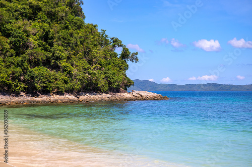 Blue sea water and white beach on sunny day. Tropical island paradise photo. Green forest jungle near seashore. Exotic place for summer vacation. South Asia travel. Tourist resort relaxing view
