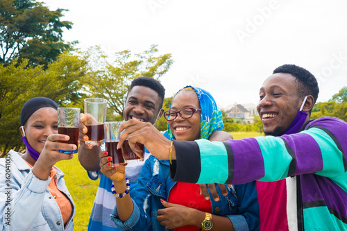 young black people standing in a park, giving a toast with drink in their glass cups