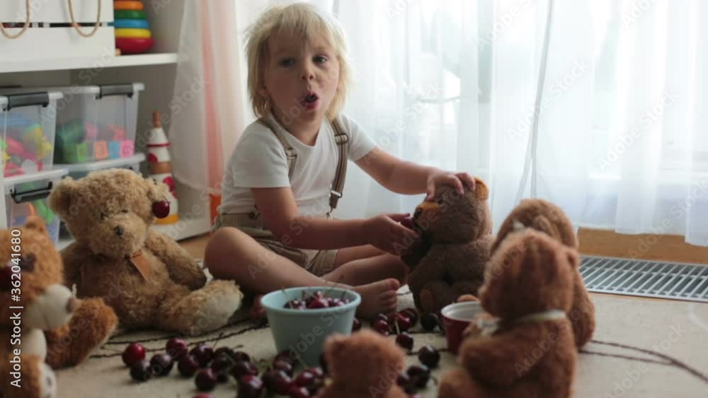 Toddler blond child, cute boy, eating cherries with teddy bears at home Toddler blond child, cute boy, eating cherries with teddy bears at home