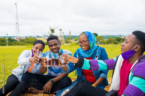 young black people sitting in a park and making a toast with drink in their cups