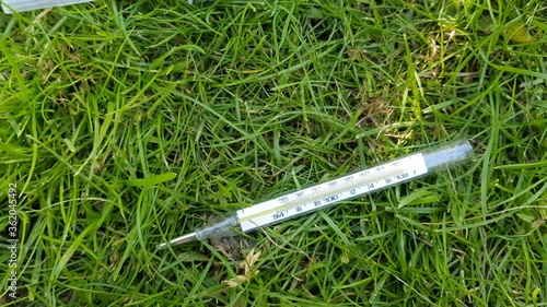 Close-up of essential drugs for the prevention of viral diseases: thermometer, disinfectant spray, syringe, medical face mask. Against the background of green grass on a sunny day