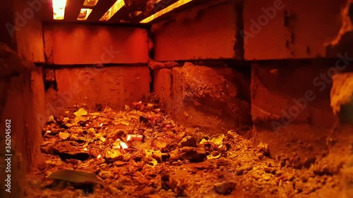 Ember red coals in the air intake of a brick kiln. Wooden firewood is burning from above. Against the background of masonry bricks, with a red tint from the fire. High temperature is generated inside.