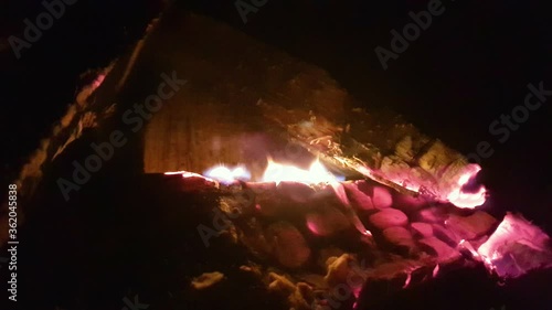 Closeup of burning firewood in the fireplace against the background of red bricks. Bright fire creates flames and shadow glare along the walls. Forms bright red coals. The feeling of comfort.