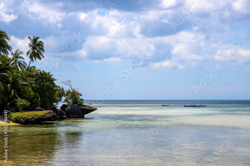Tropical island landscape with still seashore  rocks and palm tree. Tropical vacation photo. Blue sea view. Hot day on seaside. Untouched island. Marine vacation banner template. South Asia travel