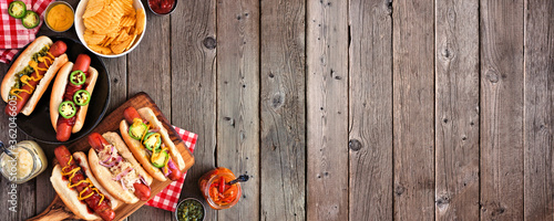 BBQ hot dog corner border. Top view table scene with a dark wood banner background. Copy space.