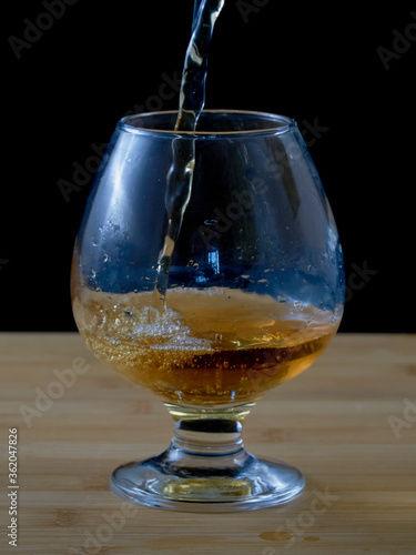 Filling a glass with fresh apple juice on a wooden surface with a black background