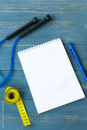 Gym exercise list mockup, dumbbells and a skipping rope on blue background