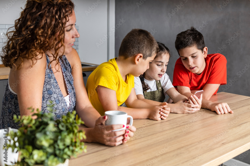Fototapeta premium Happy mother looking her children playing with the smart phone