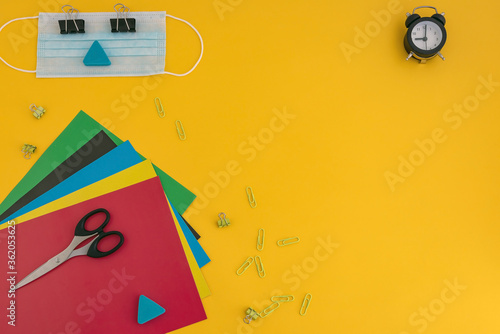 colored paper, scissors, watch, face mask, paper clips on a yellow background. back to school concept