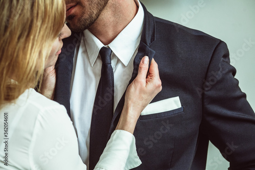 Young businesswoman holding jacket collar of businessman. Flirting couple of unrecognizable caucasian people. Passionate love affair in office workplace. Close up shot. photo