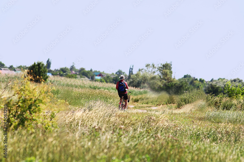 A cyclist rides to village, on a country road, among the grasses.