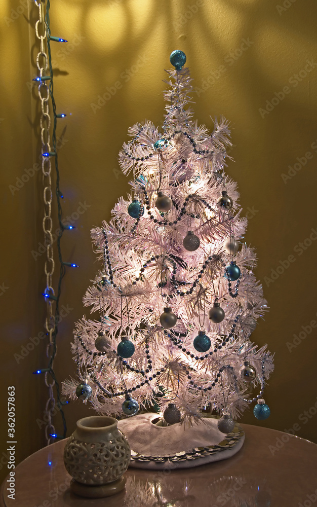 This small white table top Christmas tree is decorated with silver and blue theme.  Dramatic lighting about creates interesting shadows and effects upon the wall of this holiday image.